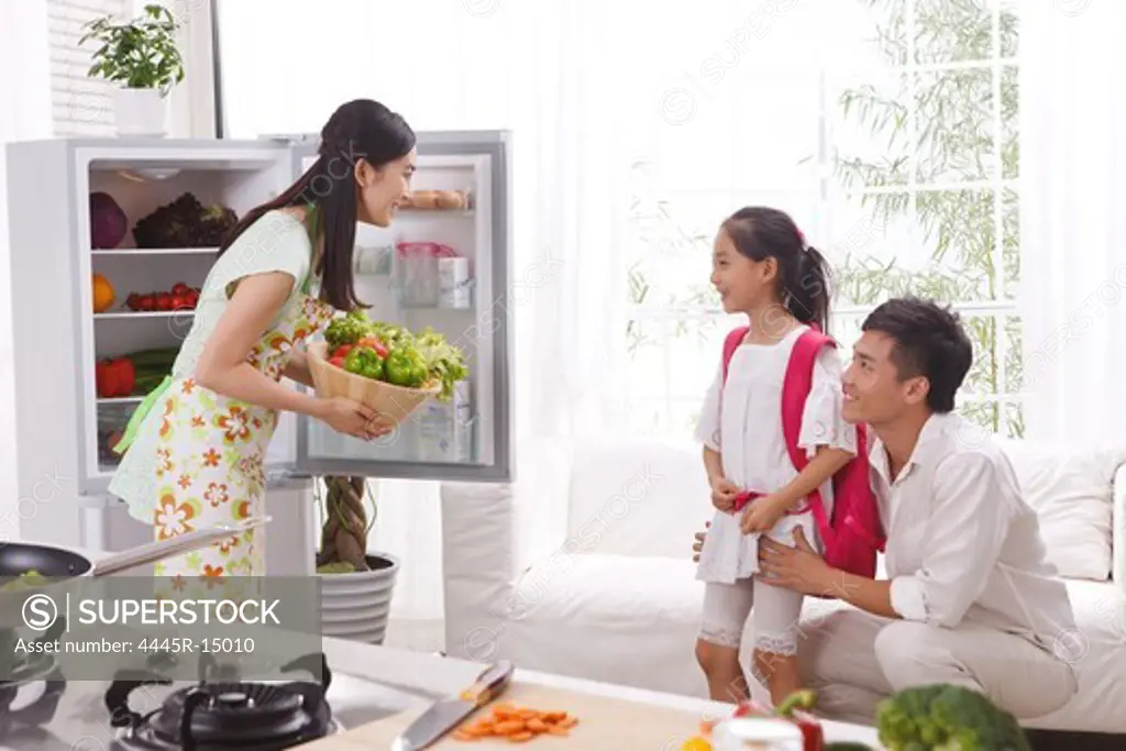 Young woman holding vegetables with family in kitchen