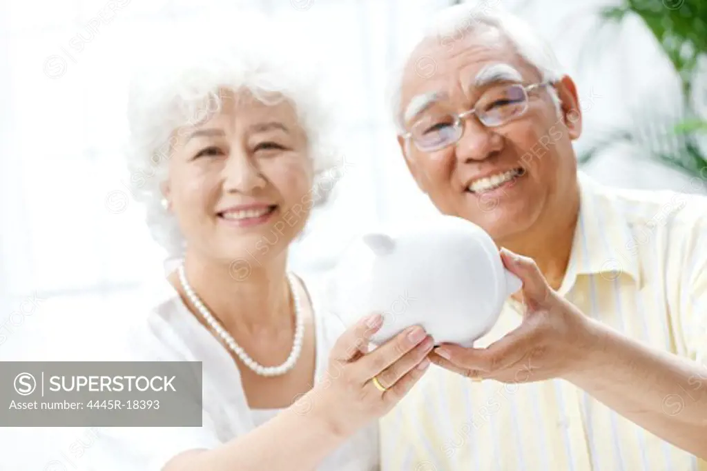 Happy elderly couple holding a piggy bank
