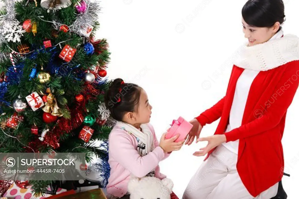Girl with mother sitting beside Christmas tree