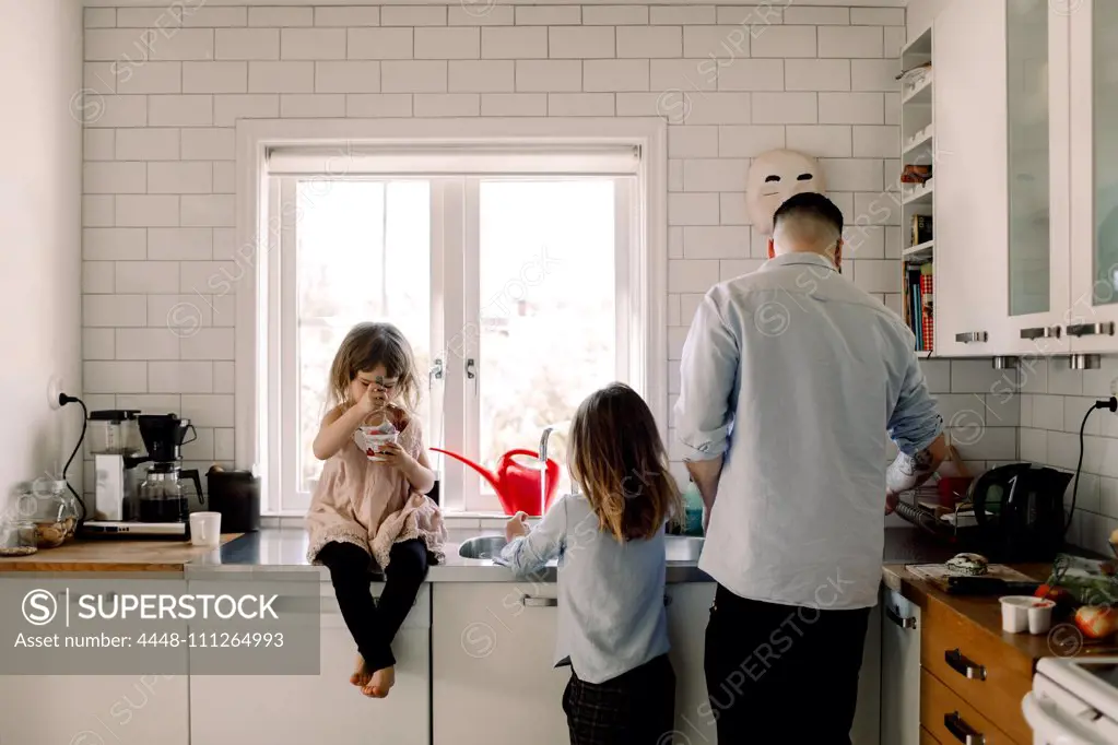 Father and daughter working while girl eating food in kitchen at home