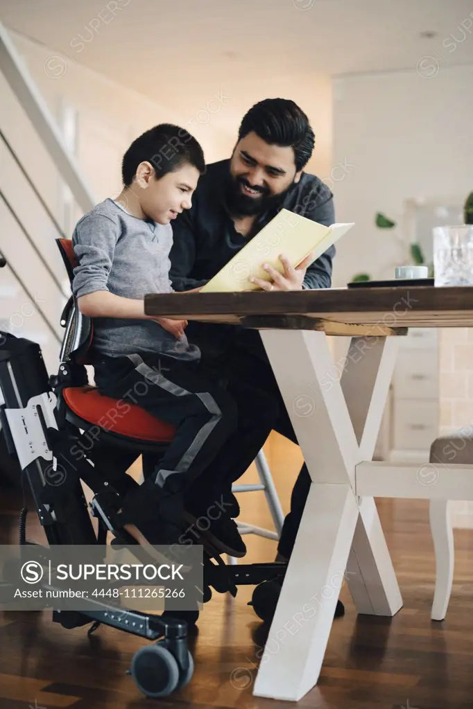 Father teaching autistic son while sitting at table in living room