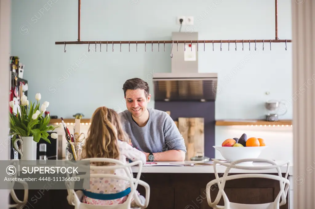 Happy father assisting daughter studying in kitchen at home