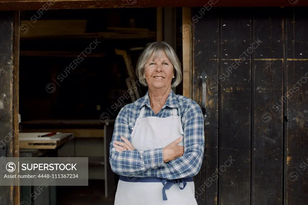 Portrait of smiling senior entrepreneur standing with arms crossed at hardware store entrance