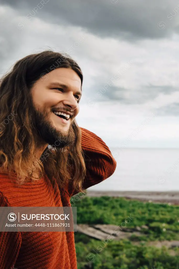 Close-up of smiling man with long hair against beach