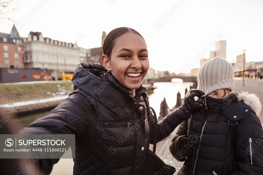 Portrait of happy teenage girl playing mischief with friend in city