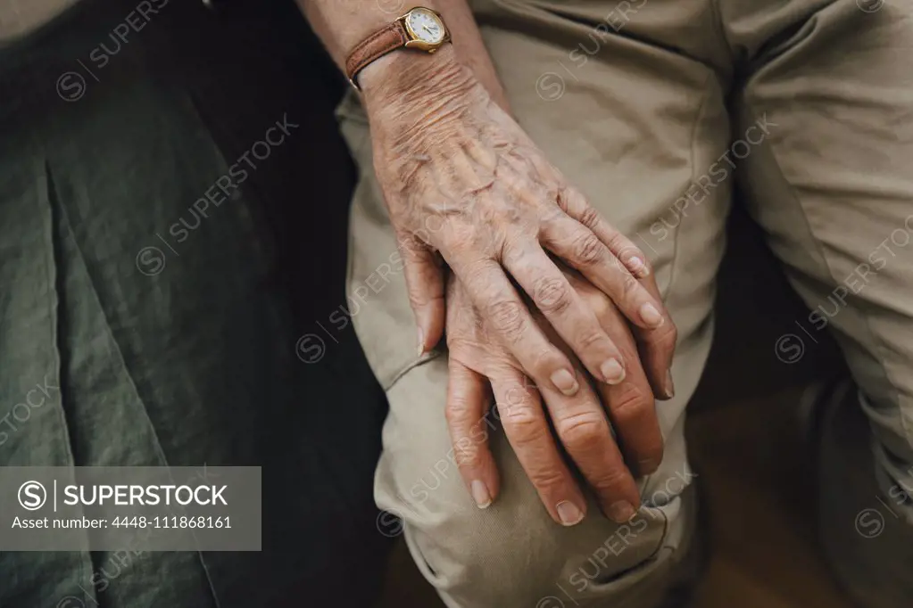 Midsection of retired senior couple holding hands sitting at nursing home
