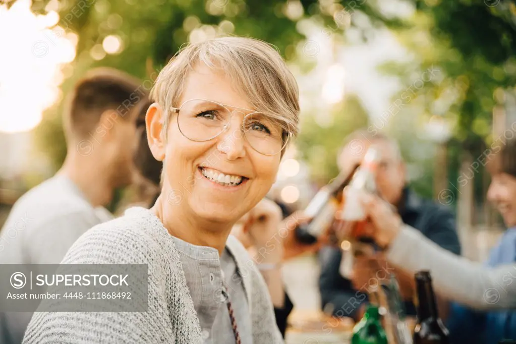 Portrait of happy mature female sitting with friends at social gathering