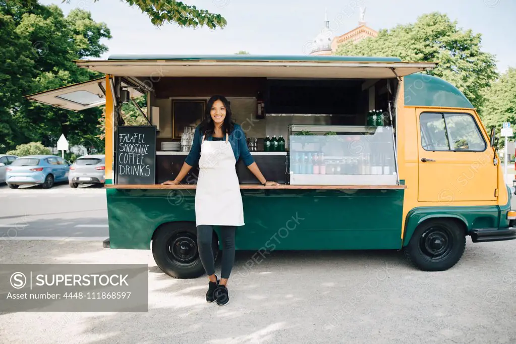 Portrait of smiling female owner standing against food truck