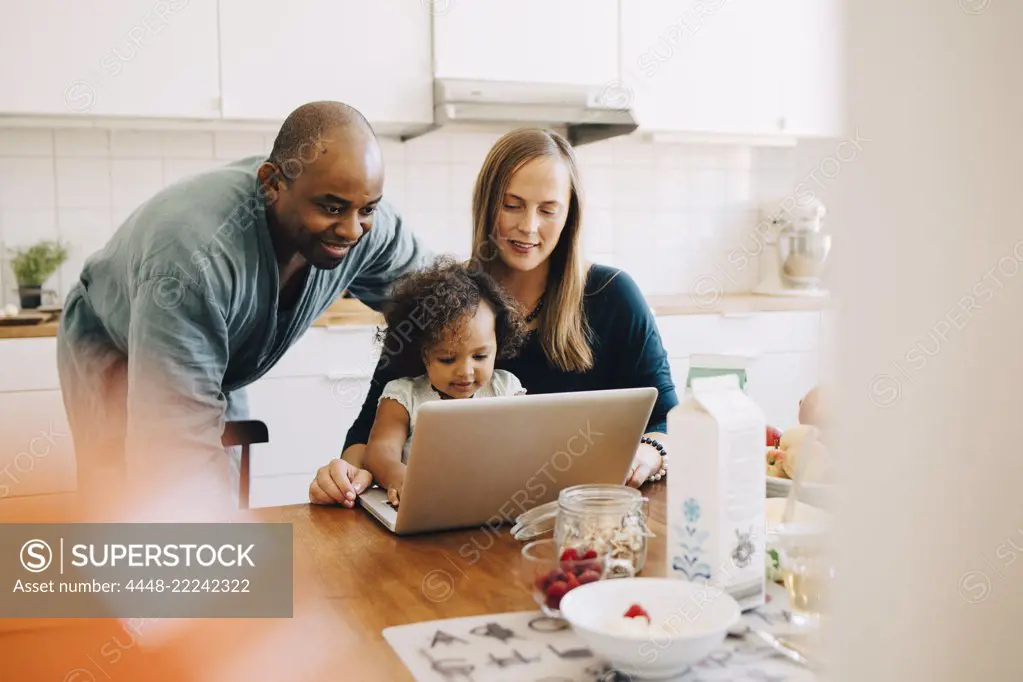 Smiling parents looking at daughter playing with laptop in dining room