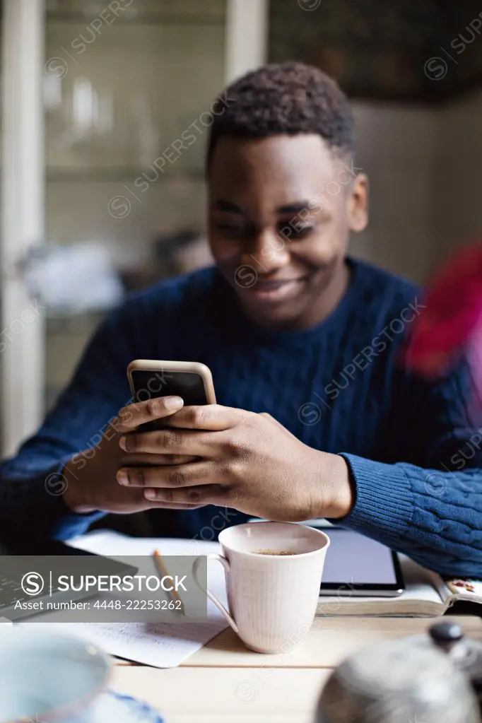 Smiling teenage boy using social media on smart phone while studying at home