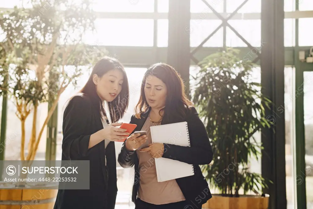 Confident female colleagues discussing over smart phones at office