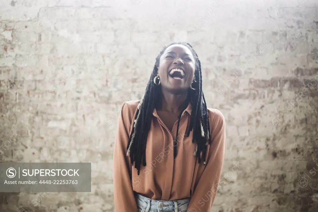 Female computer hacker with dreadlocks laughing against wall in office