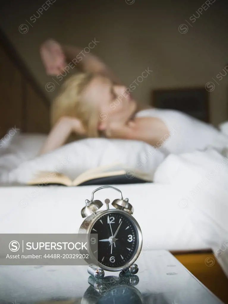 Woman in her bed with clock and book