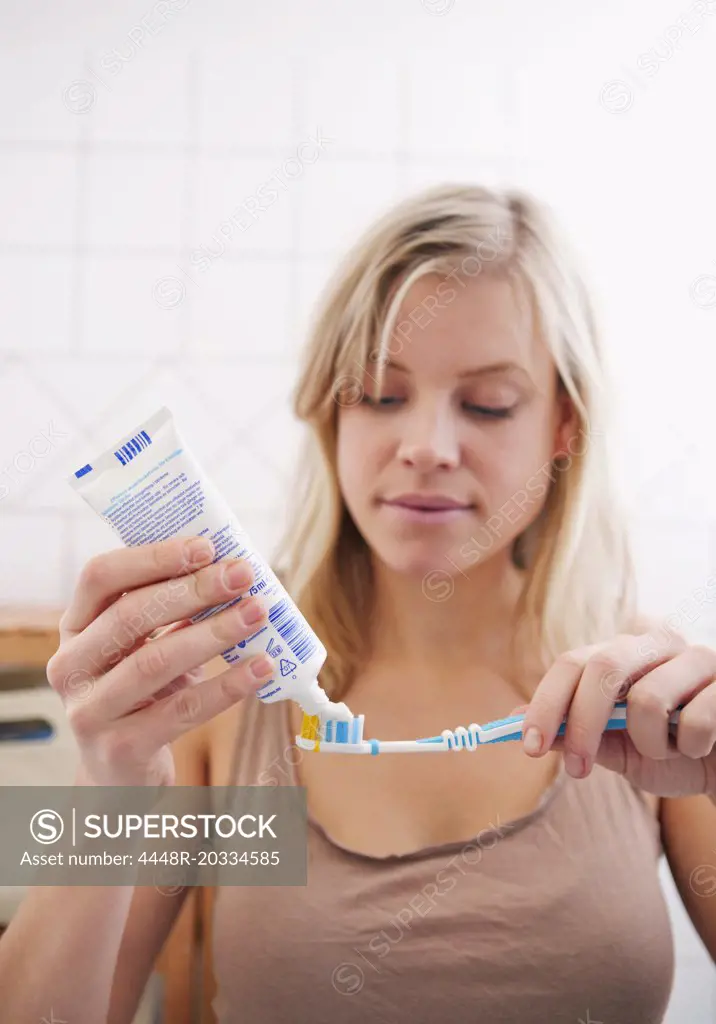 Woman standing in bathroom with toothpaste and toothbrush