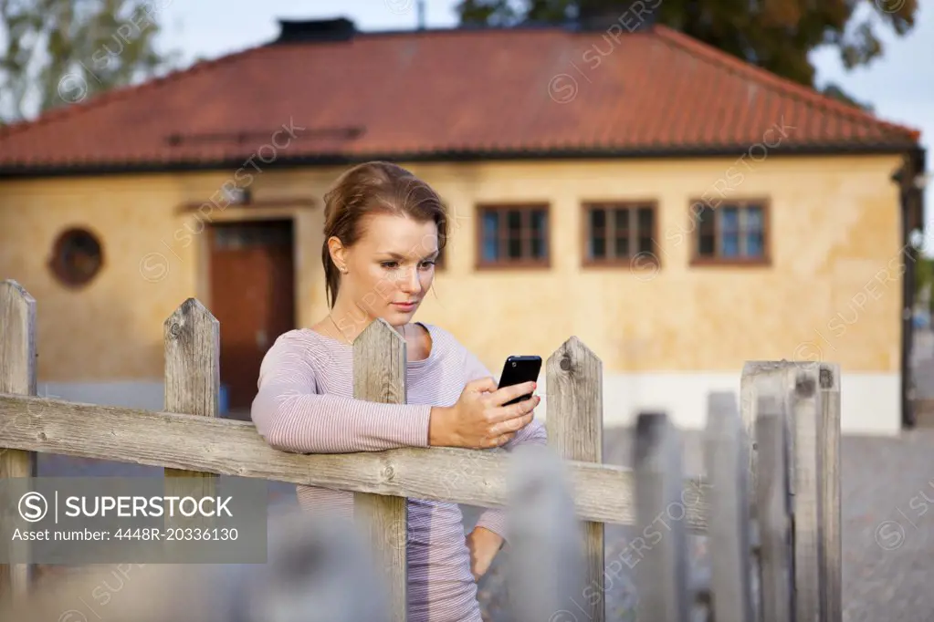 Girl leaning against fence with cellphone in her hand
