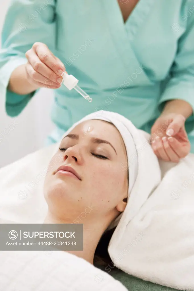 Massage therapist applying oil from pipette on young woman's forehead