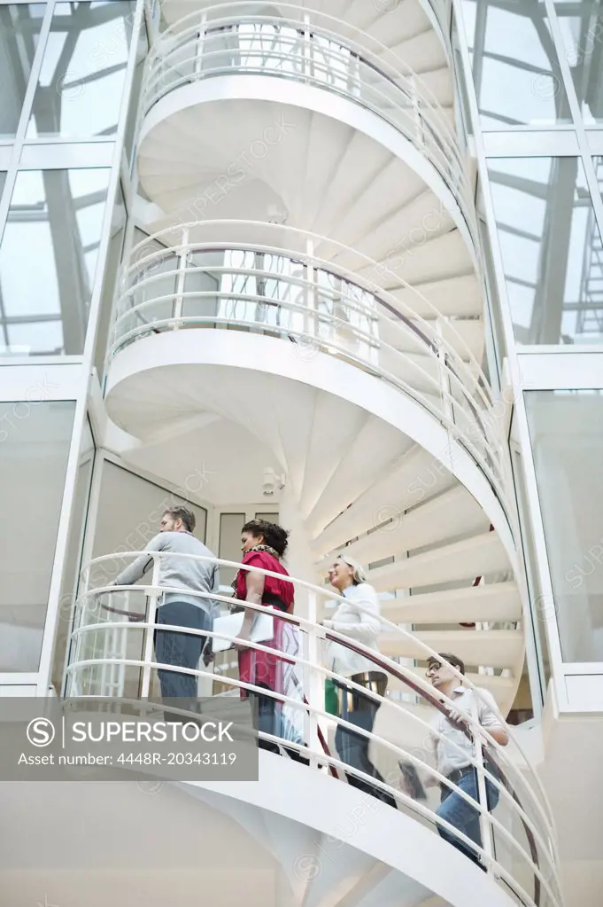 Four business people climbing spiral staircase in office