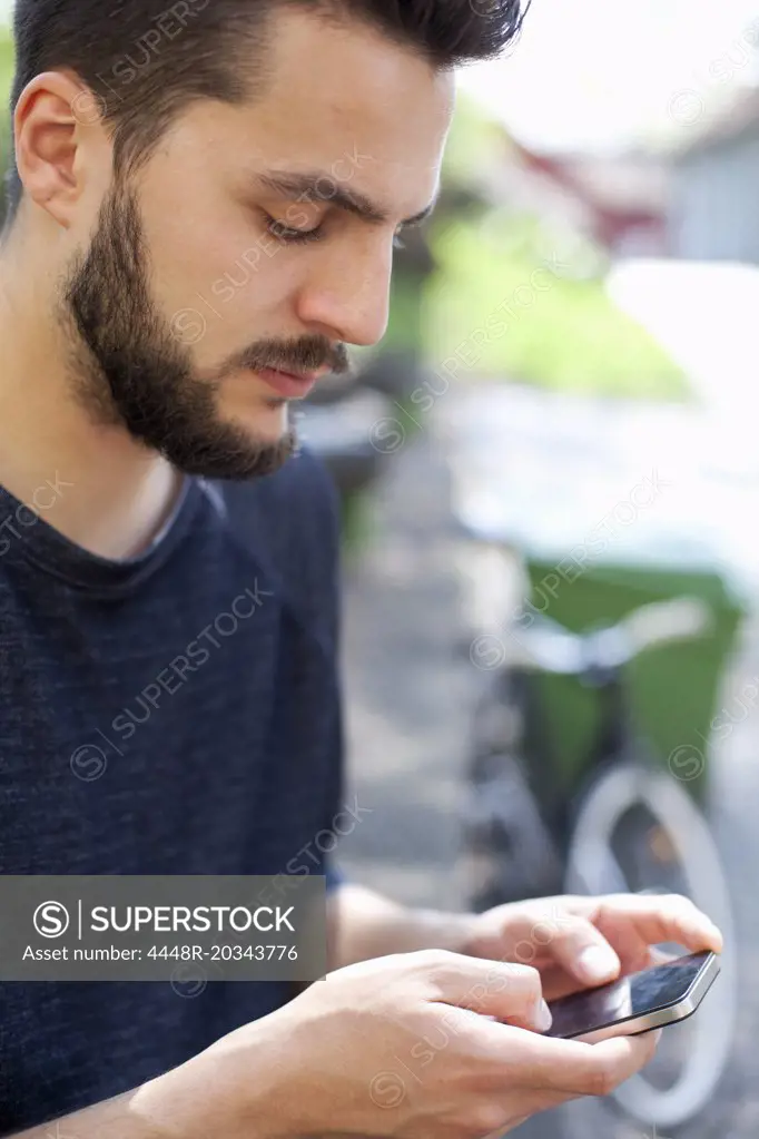 Young man text messaging on mobile phone at park