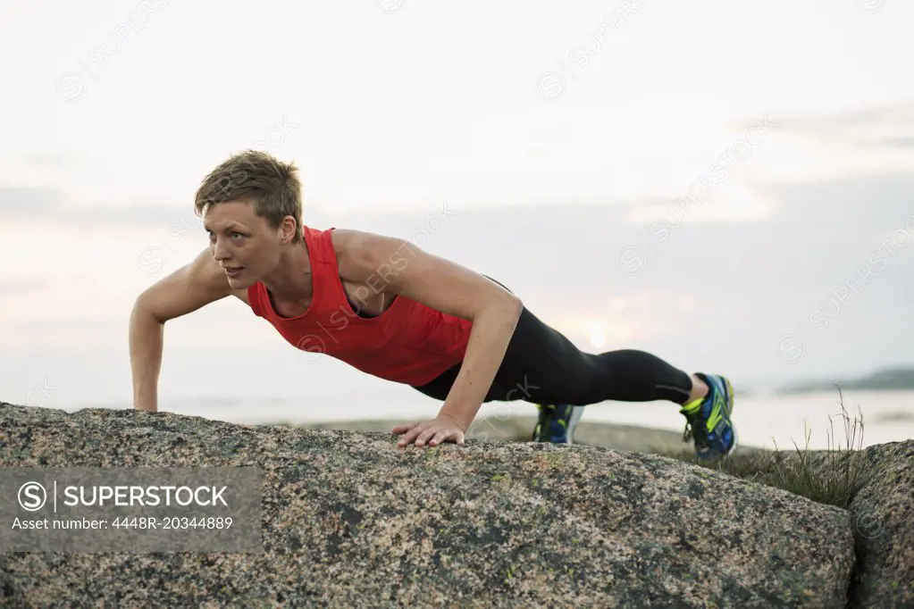 Sporty woman doing pushups on rock