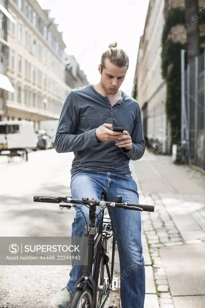 Young man using mobile phone while sitting on bicycle at street