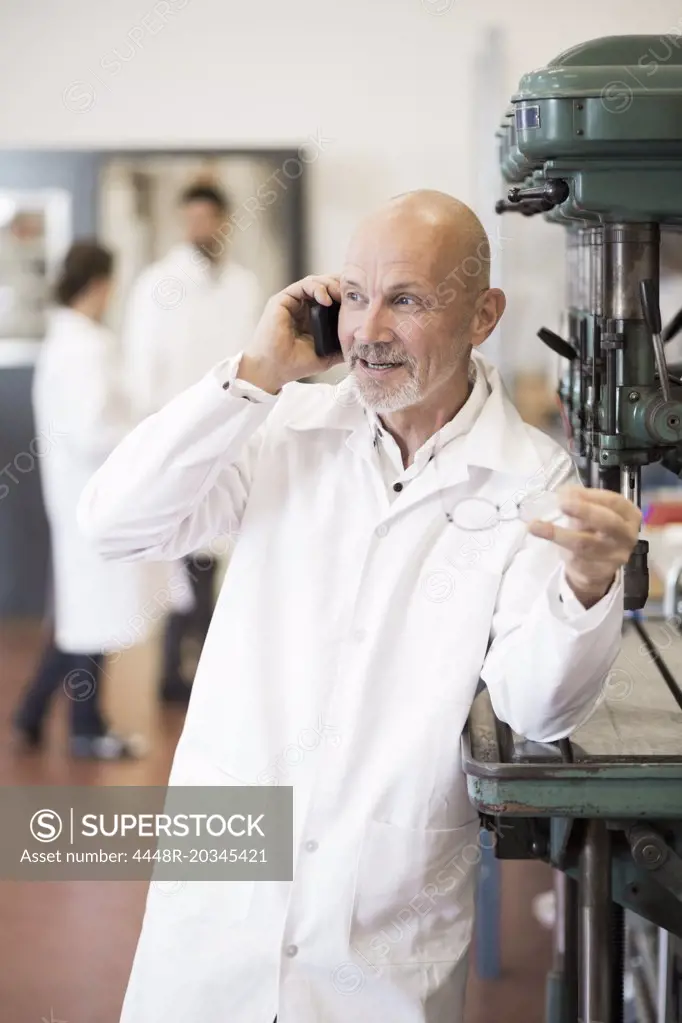 Engineer answering mobile phone with colleagues in background at industry