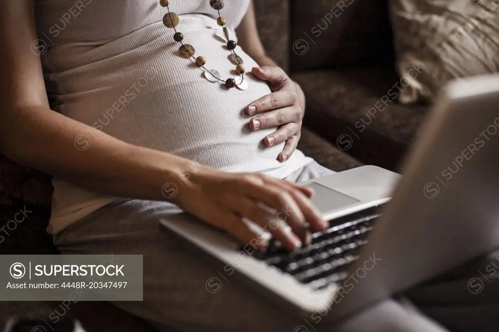 Midsection of pregnant woman using laptop at home
