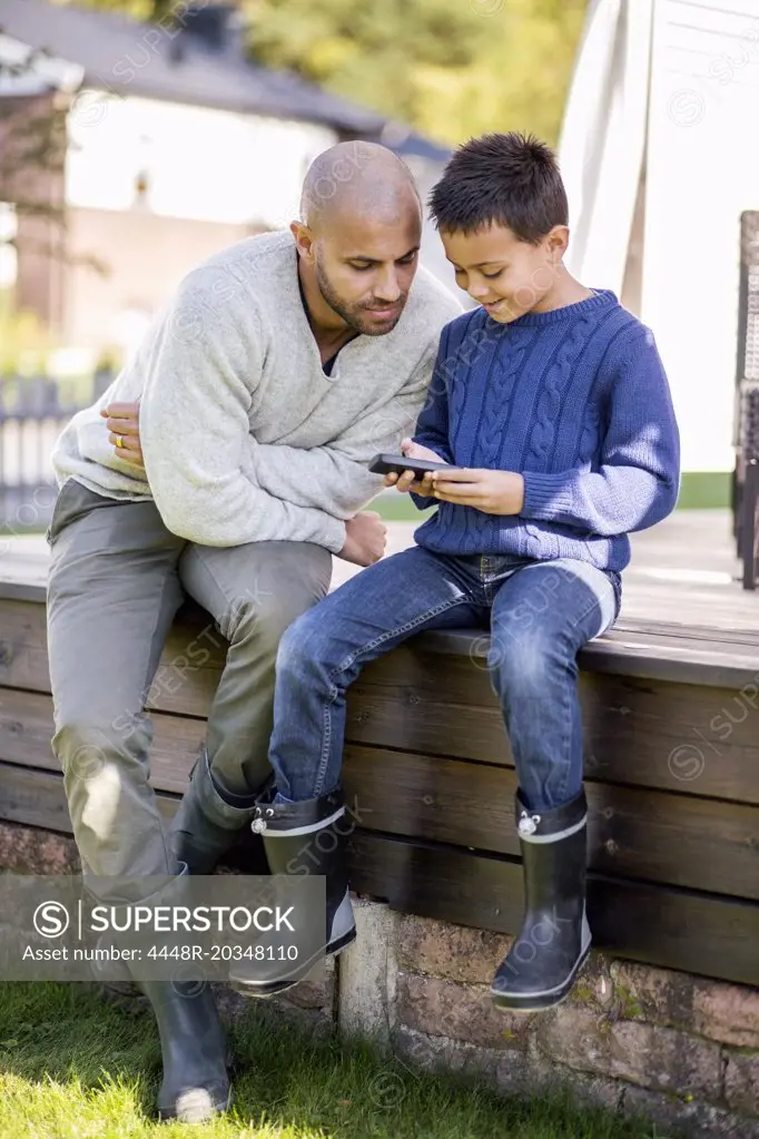 Father and son using mobile phone at yard