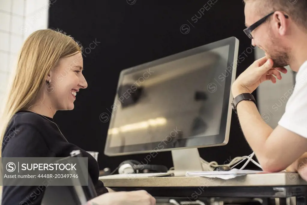 Young businessman and businesswoman looking at computer monitor in creative office