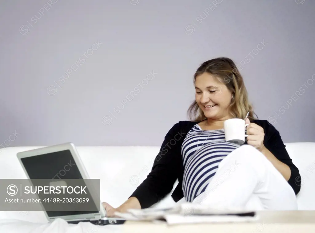 Young pregnant woman sitting in a couch with a laptop