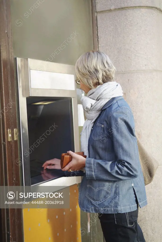 Girl in jeans jacket getting cash from ATM machine