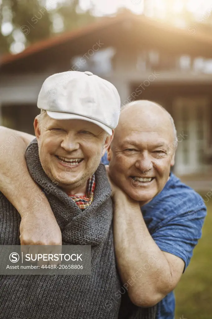 Portrait of happy gay man leaning on partner's shoulders at yard