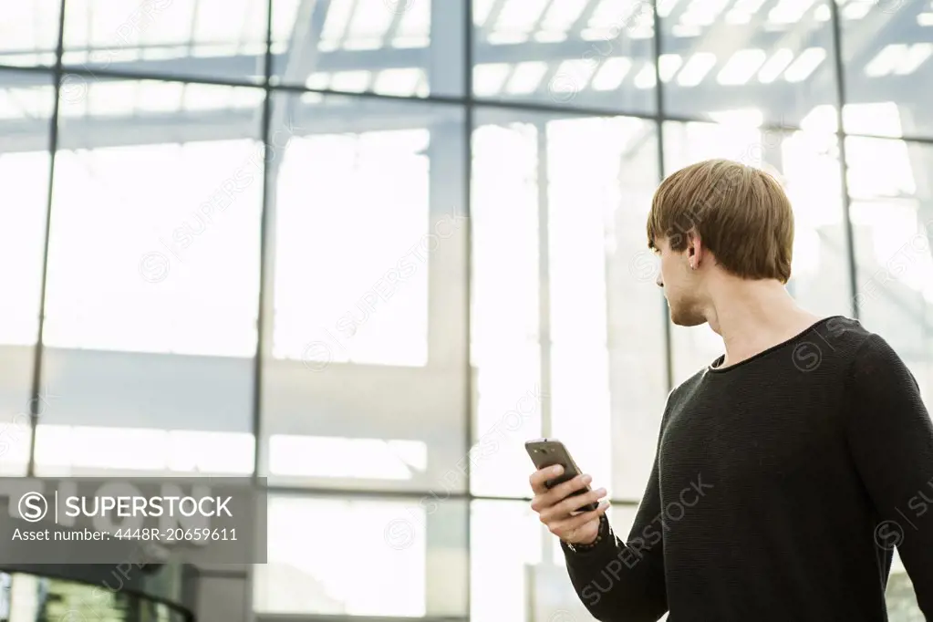 Man holding smart phone while looking at station building