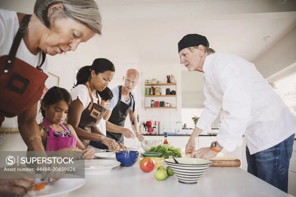 Senior man guiding family in preparing Asian food at kitchen