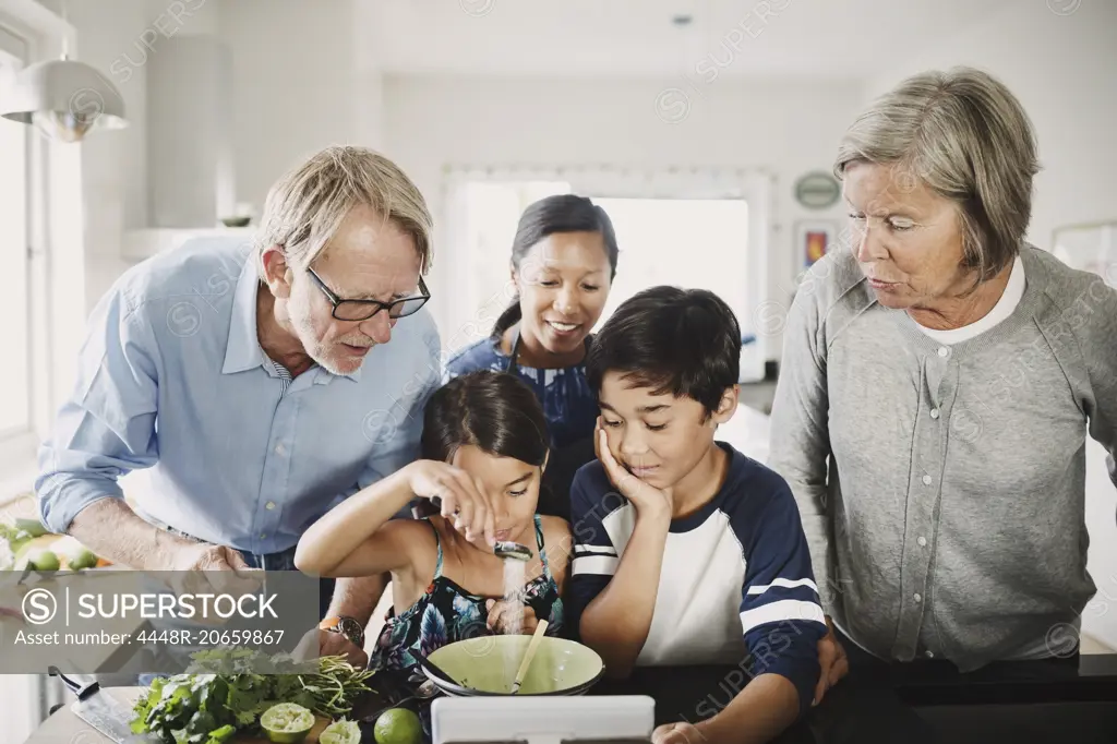 Family looking at girl preparing food at kitchen counter
