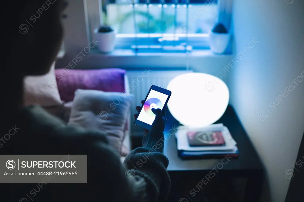 Cropped image of teenage girl using smart phone while standing by illuminated bed in room