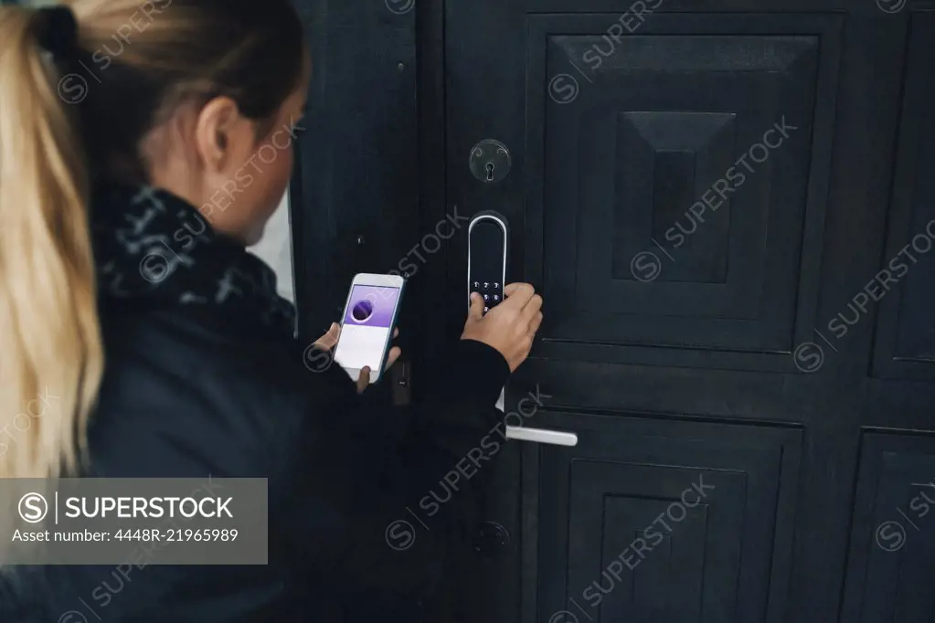 Rear view of teenage girl using smart phone to unlock house door
