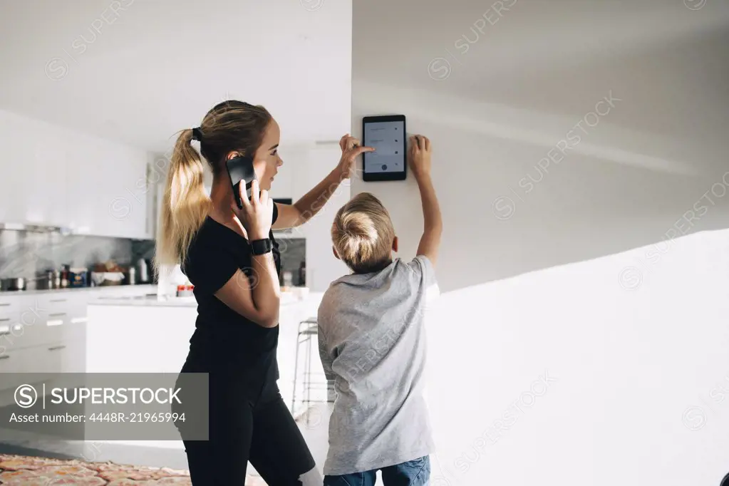 Teenage girl talking on phone using digital tablet by brother standing at home