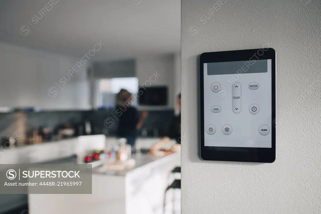 Thermostat app on digital tablet mounted over white wall at home