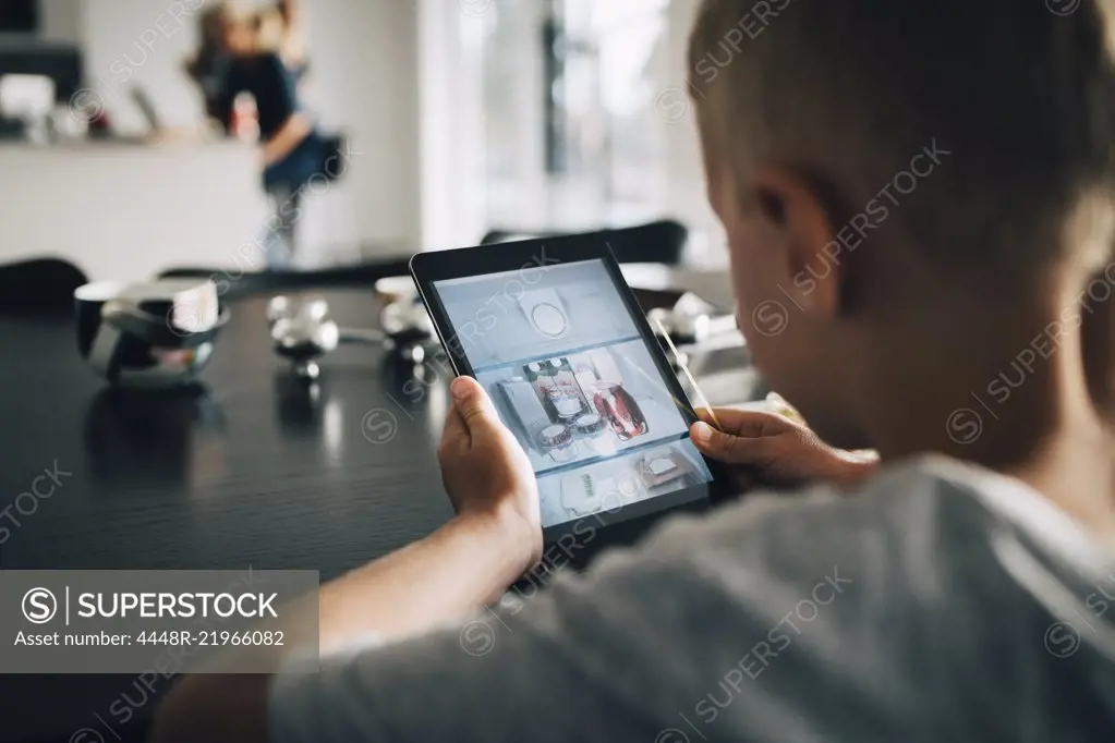 Rear view of boy using digital tablet at home