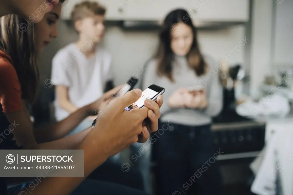 Close-up of friends using mobile phones at kitchen