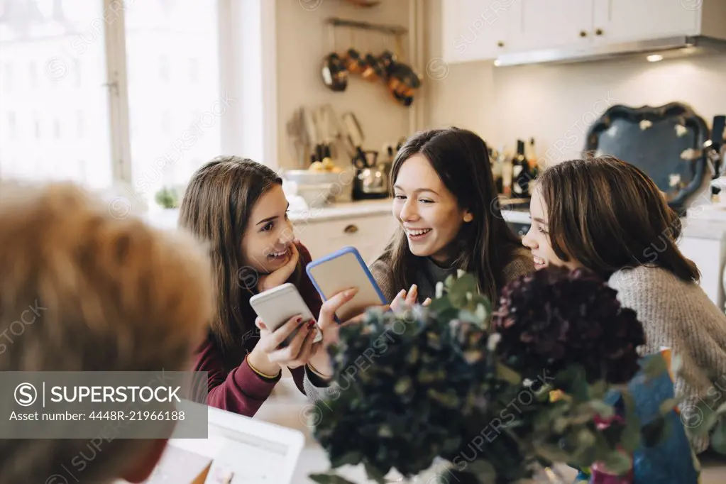 Smiling girls using mobile phone while sitting at table in room