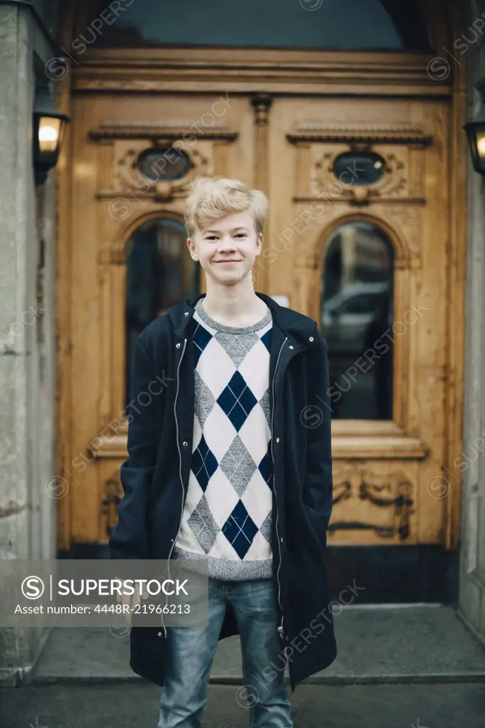 Portrait of smiling teenage boy with mobile phone standing against building