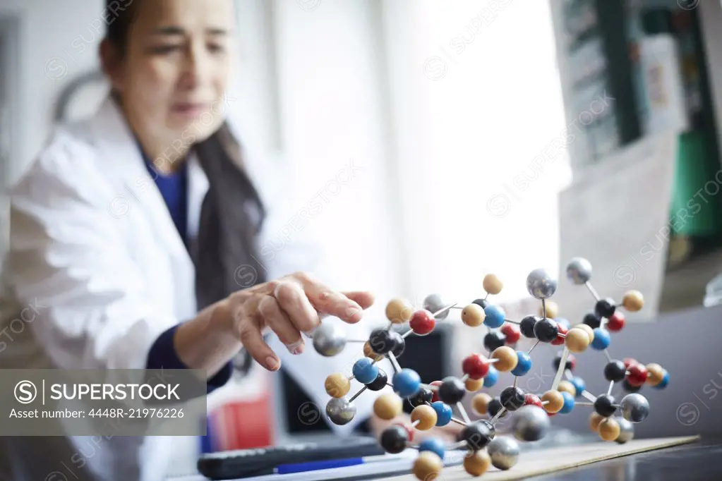 Mature teacher touching molecular structure on table at university chemistry laboratory