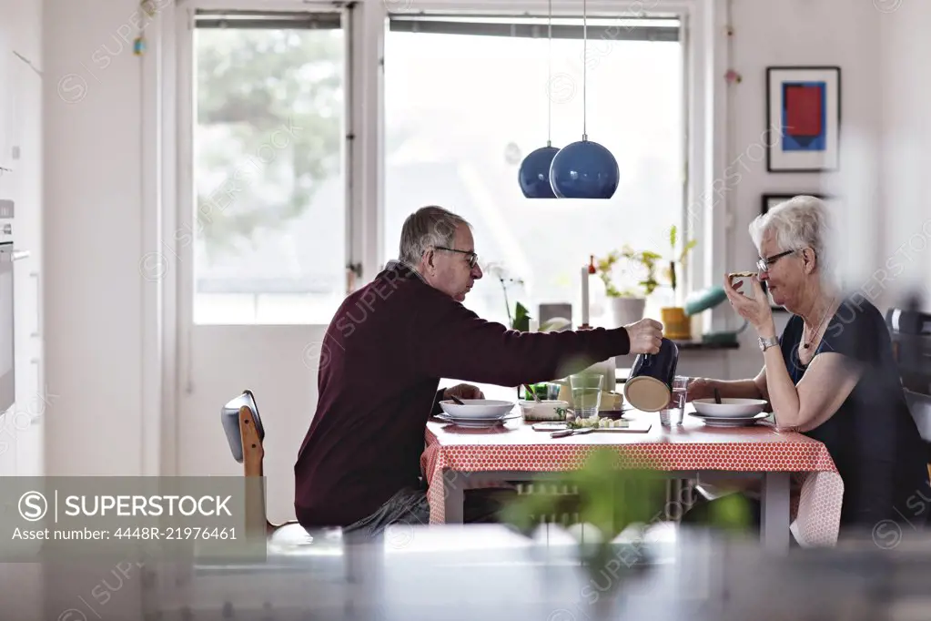Side view of senior couple eating food at dining table against window