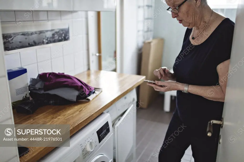 Senior woman standing in bathroom using mobile phone at home