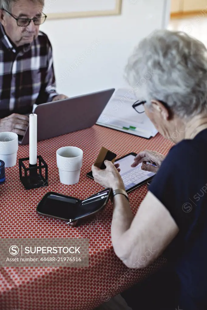 Senior woman holding credit card while using digital tablet at dining table