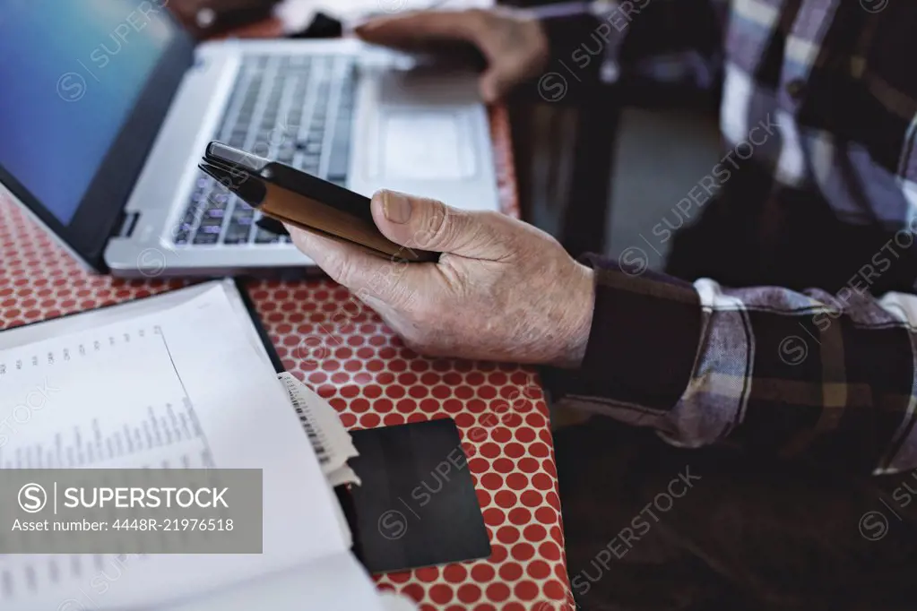 Midsection of retired senior man paying bills through credit card while using technologies at dining table