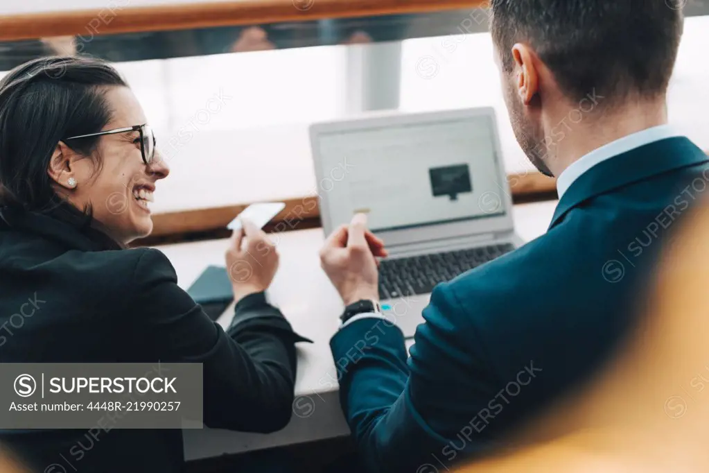 Happy businesswoman holding credit card while businessman using laptop in airport