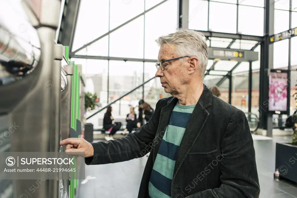 Senior male commuter using kiosk at railroad station