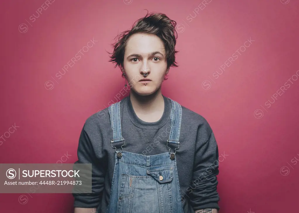 Portrait of shocked young man wearing overalls against pink background